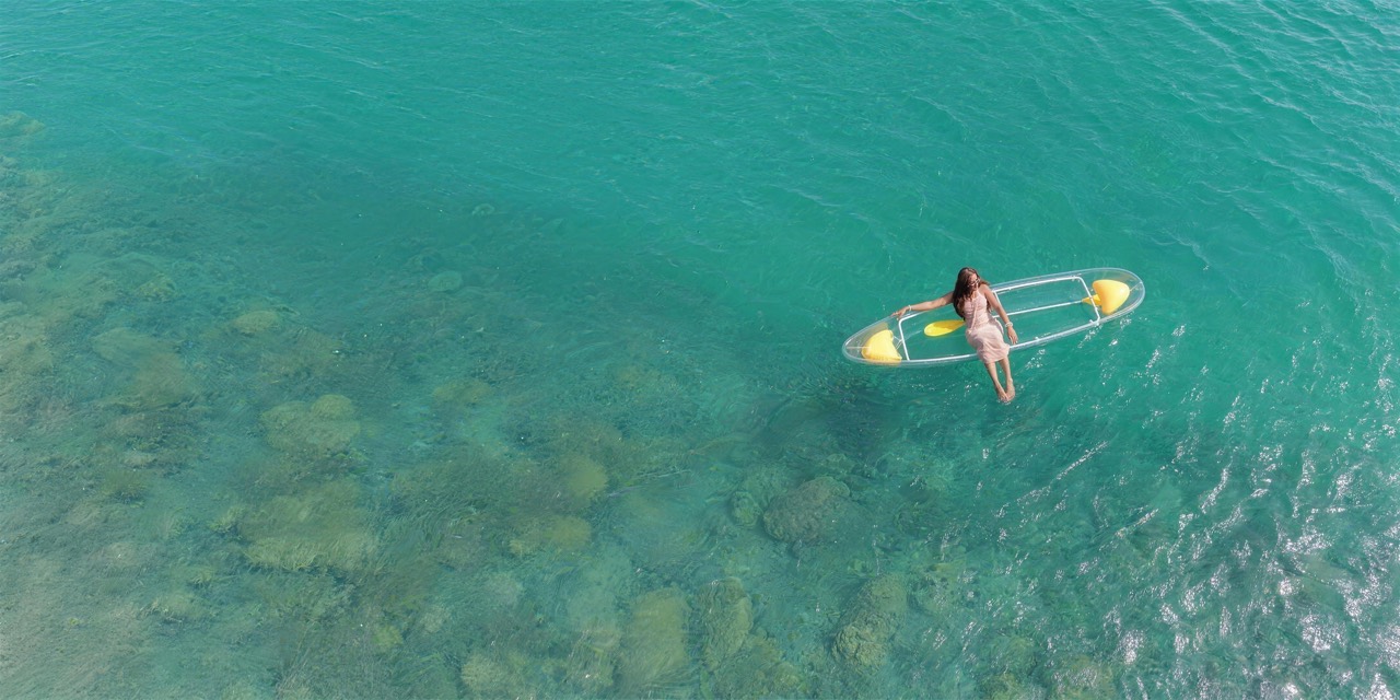 Miss Sénégal-France 2026 assise dans un kayak transparent sur l’eau turquoise de Dakar, au-dessus des rochers