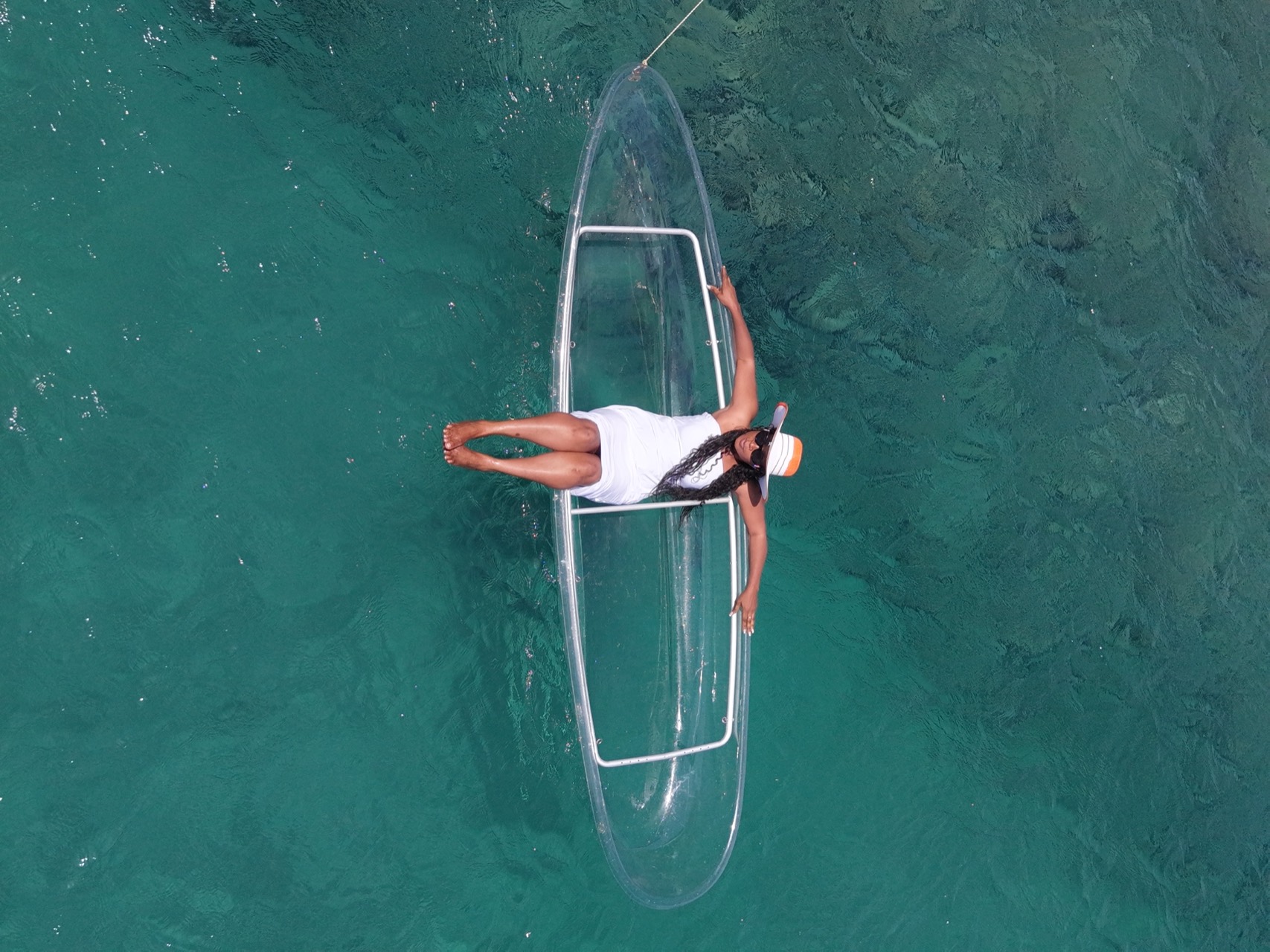Young woman in a hat lying arms open in a clear kayak on the turquoise water of Ouakam - Drone photoshoot Dakar, Senegal Nautique